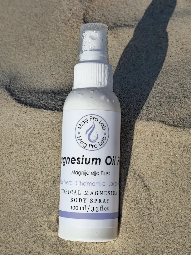 MagPro Lab Magnesium Oil Plus 100 ml | Magnija eļļa Pluss ar Alveju, Kumelīti un Lavandu MagPro Lab Magnesium Oil Plus bottle in sand for Athlete application after exercise | Magnija eļļa Pluss pudelīte smiltīs, paredzēta lietošanai pēc treniņa